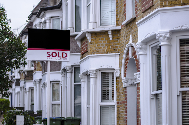 A row of terraced houses in the UK with bay windows are shown with a 'Sold' sign outside them.